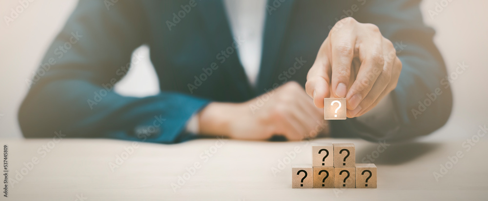 Hand hold Wooden cube block in question mark mean what on cement table background, column of wooden 