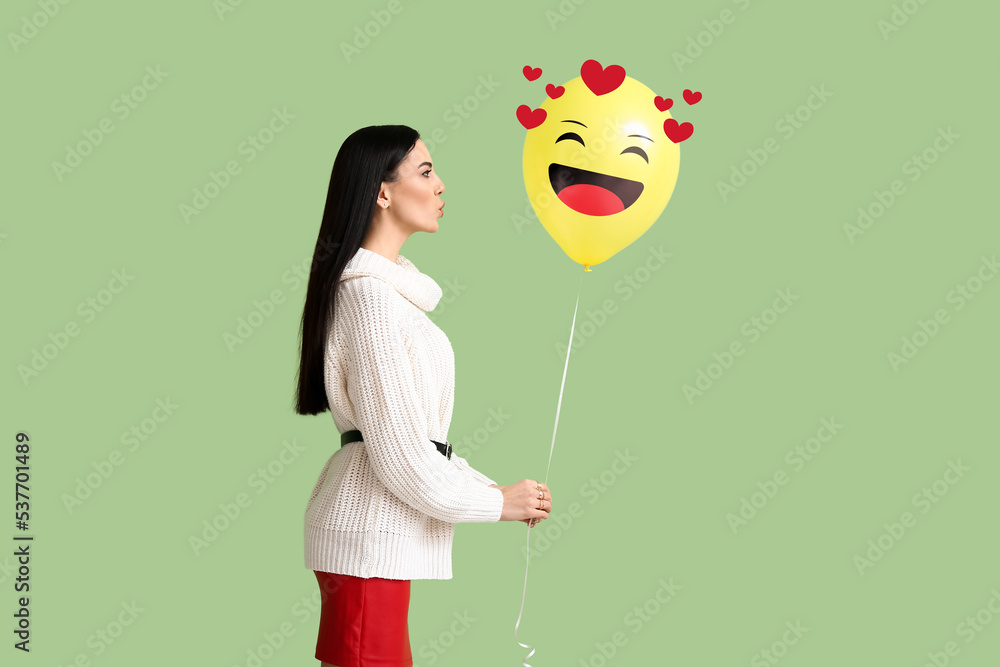 Beautiful young woman holding balloon with drawn smile on green background