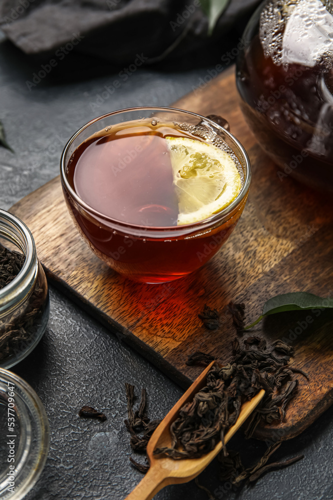 Board with glass cup of black tea and lemon on dark background, closeup