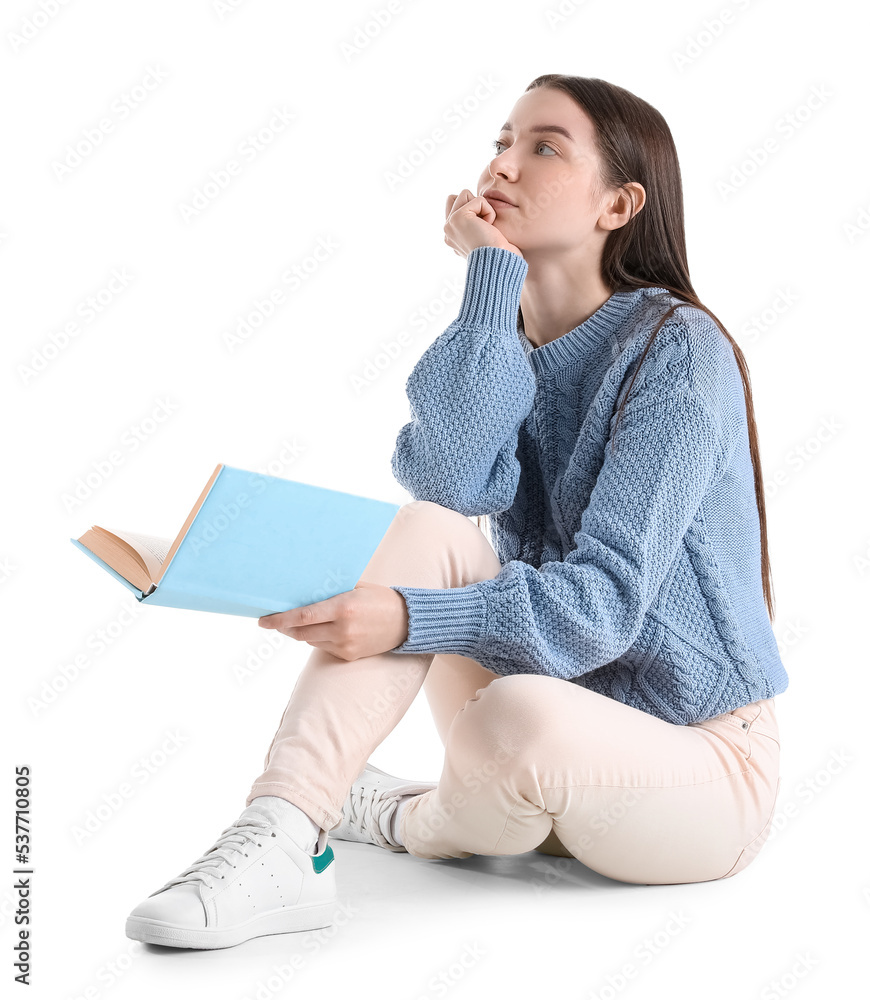 Thoughtful young woman in blue sweater with book sitting on white background