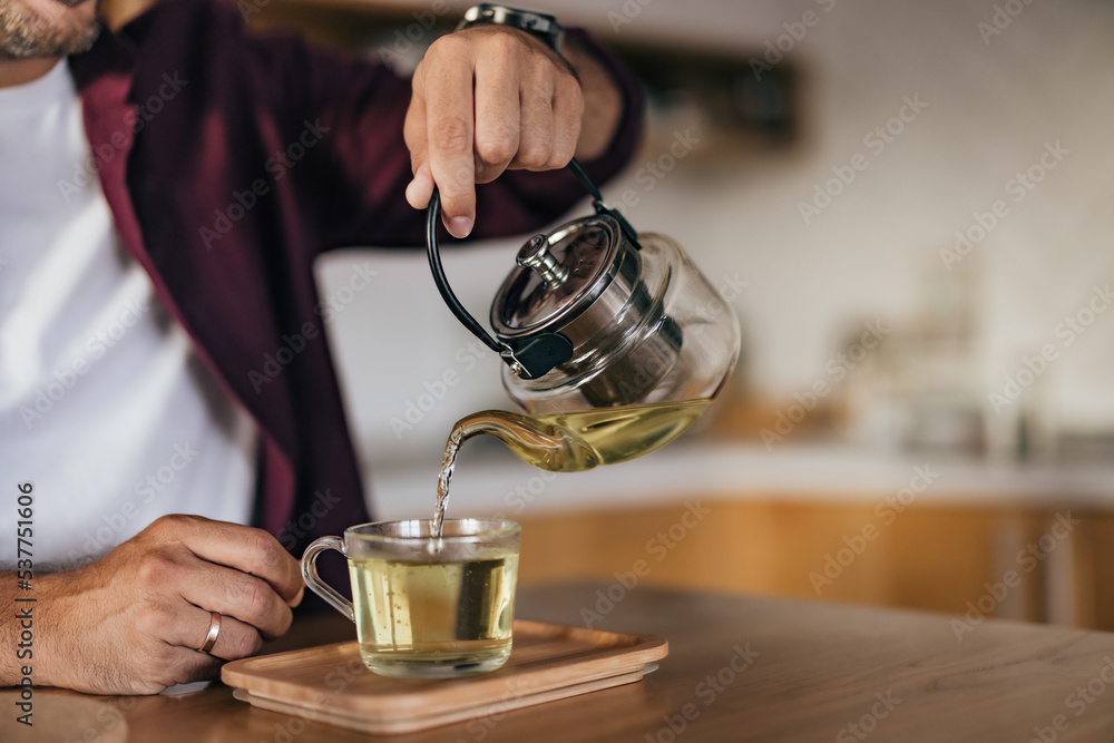 男人拿着茶壶，倒进杯子里，独自享受下午，喝茶。