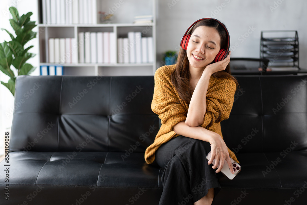 Portrait of a happy young Asian woman listening music with wireless headphones from music applicatio