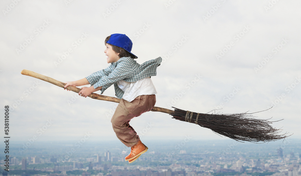 Happy boy is flying on a broomstick like a wizard. A childs fantasy. Childhood.