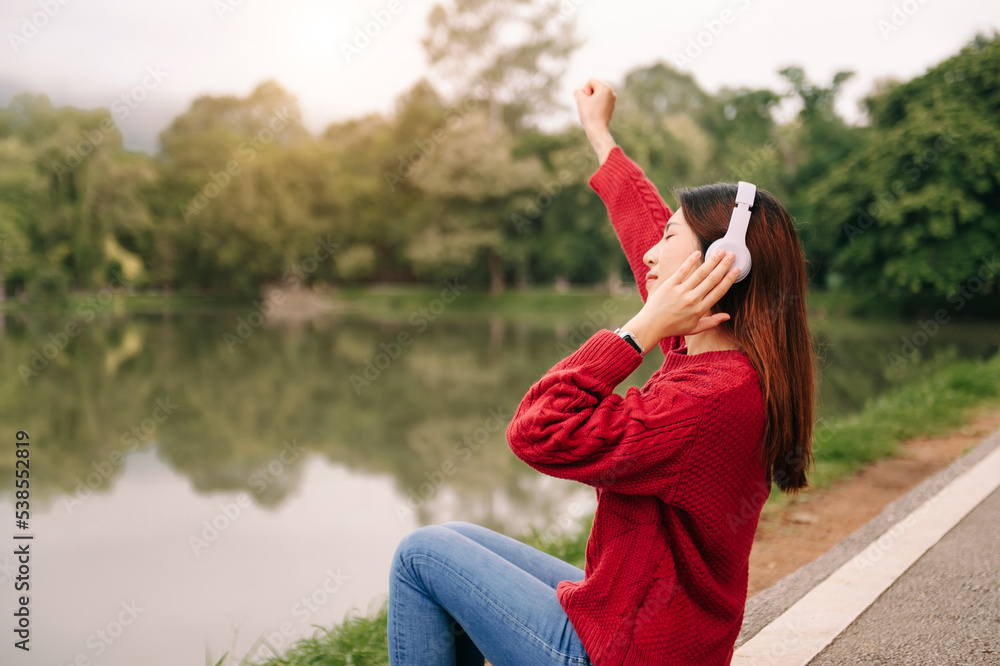 年轻的亚洲女性戴着耳机听音乐，心情愉悦、放松，笑容清新