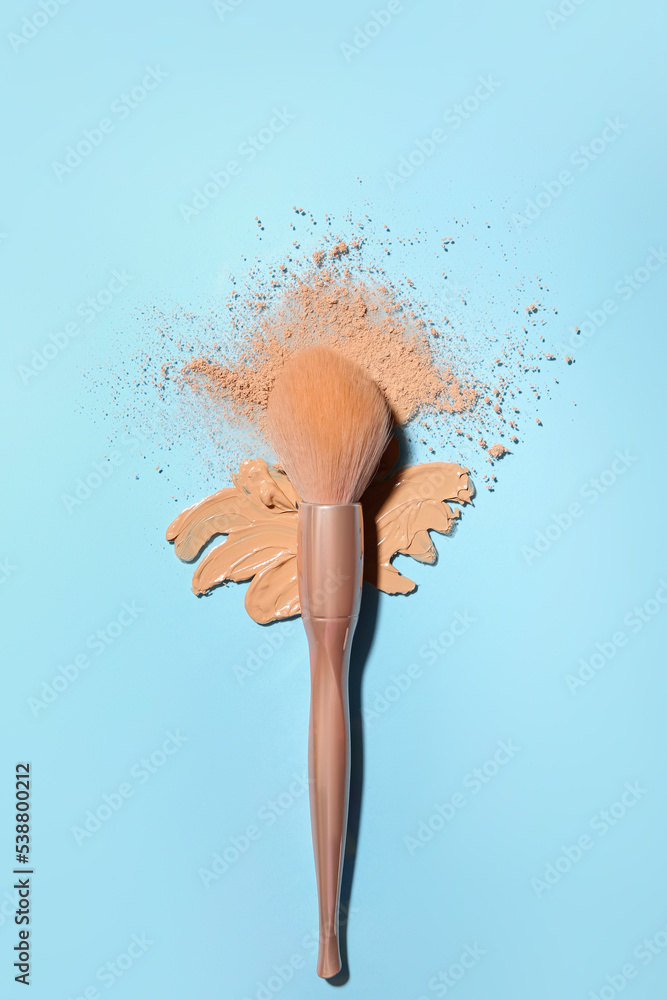 Smear of makeup foundation with powder and brush on blue background