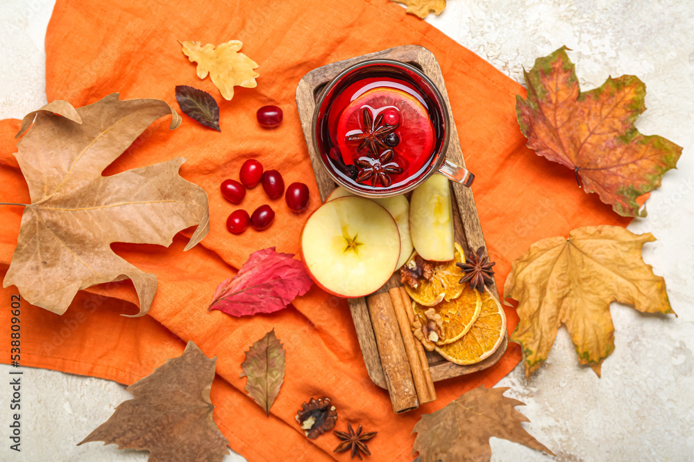 Composition with cup of aromatic mulled wine, fruits, spices and autumn leaves on light background