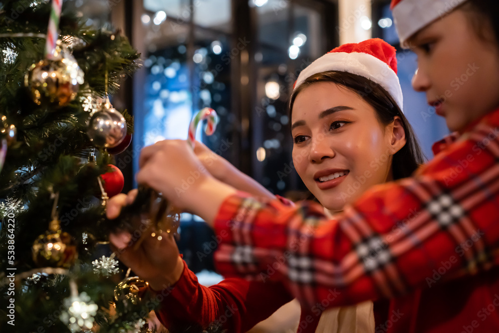 Asian beautiful mother and daughter decorating Christmas tree at home. 