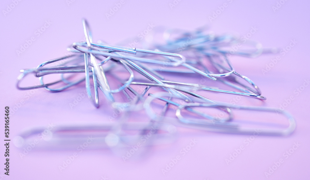 Paper clips together in pile, connected and a chain on purple background. Office supplies, organizat