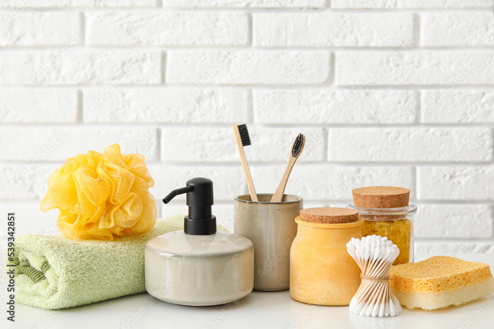 Set of bath supplies on table against light brick wall