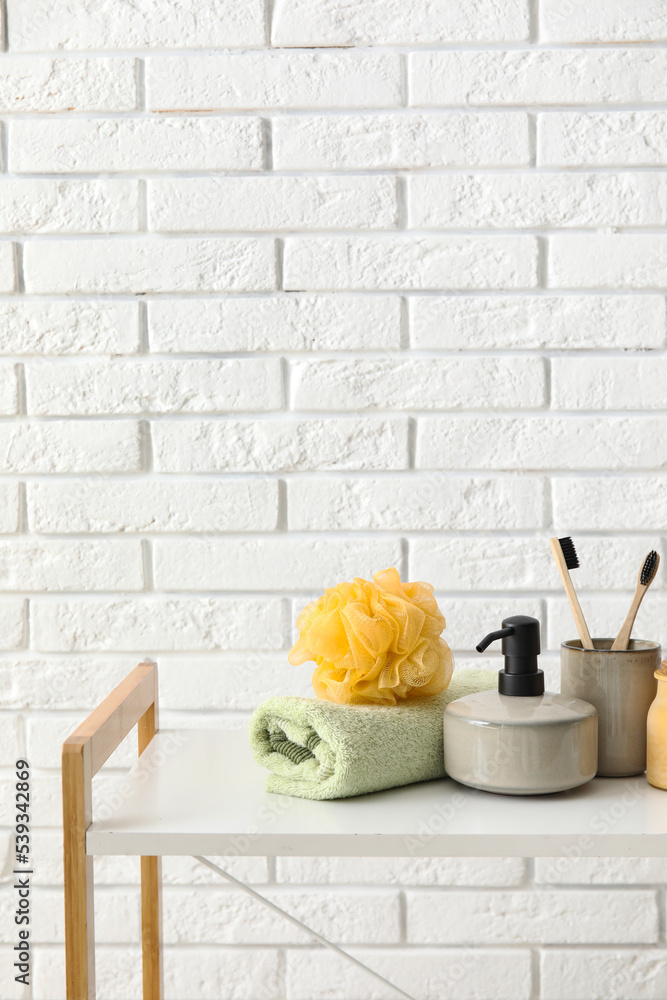 Set of bath supplies on table against light brick wall