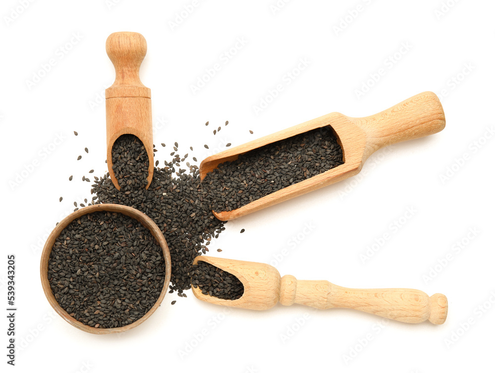 Wooden bowl and scoops with black sesame seeds on white background