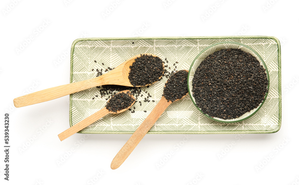 Plate with spoons of black sesame seeds on white background