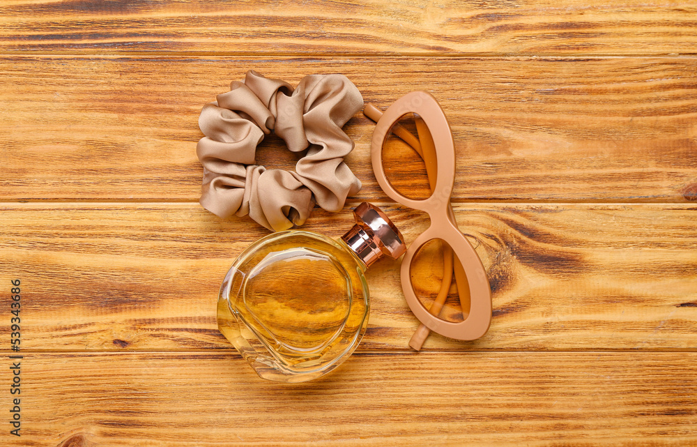 Perfume bottle, sunglasses and silk scrunchy on wooden background