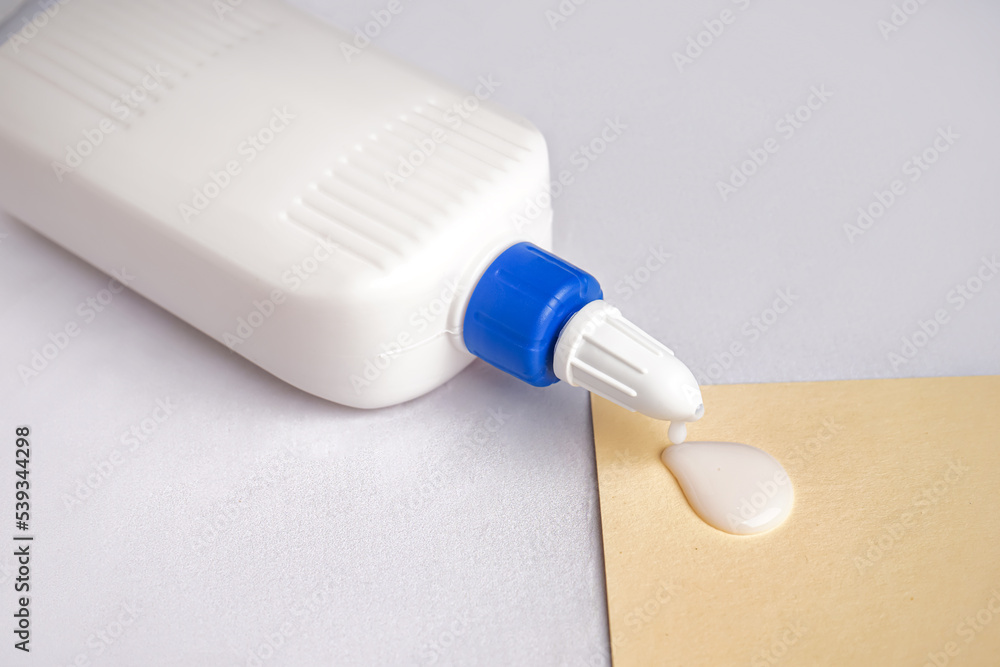 Bottle of glue and paper sheet on light background, closeup