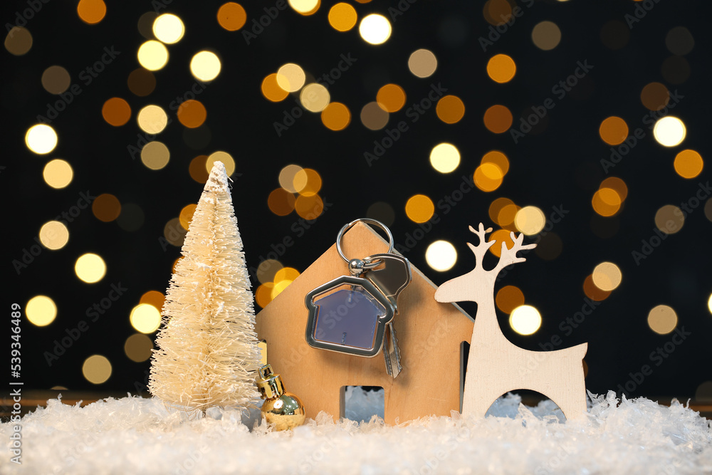 House figure with key and Christmas decor on snow against blurred lights