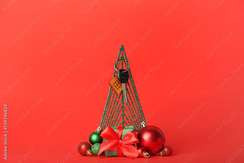 Key from new house with Christmas decor and gift on red background