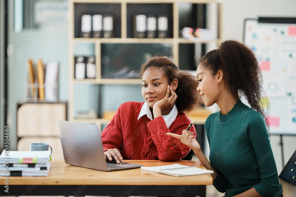 Focused young african american businesswoman or student looking at laptop holding book learning, ser