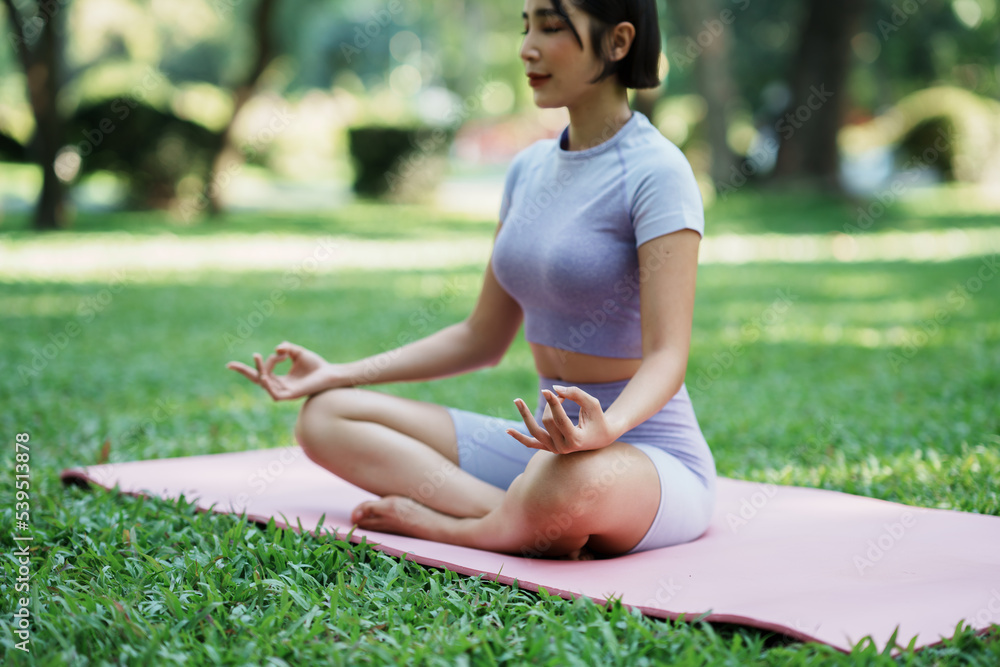 美丽的年轻亚洲女性在公园里做瑜伽运动。