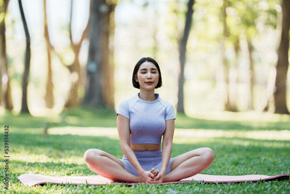 美丽的年轻亚洲女性在公园里练习瑜伽。