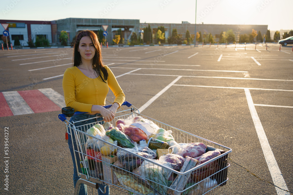 超市附近停车场，年轻女子拿着装满新鲜健康食品的购物车