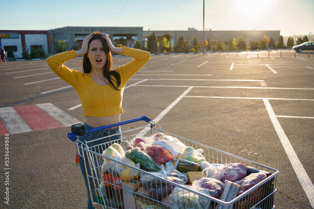 Young woman with shopping cart full of fresh and healthy food on the parking place near the supermar