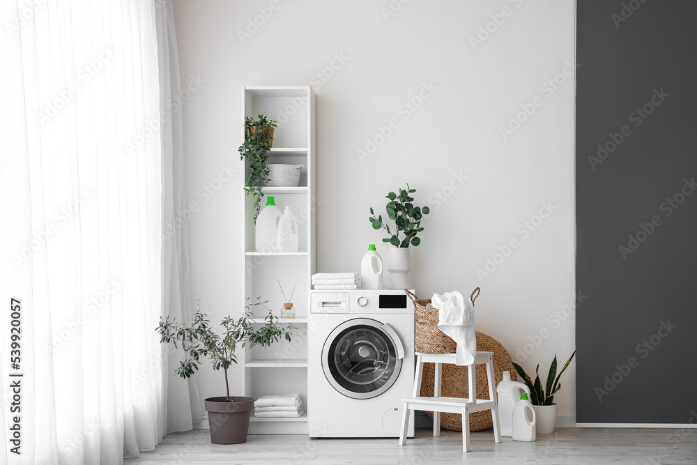 Interior of light laundry room with washing machine, shelving unit and houseplants