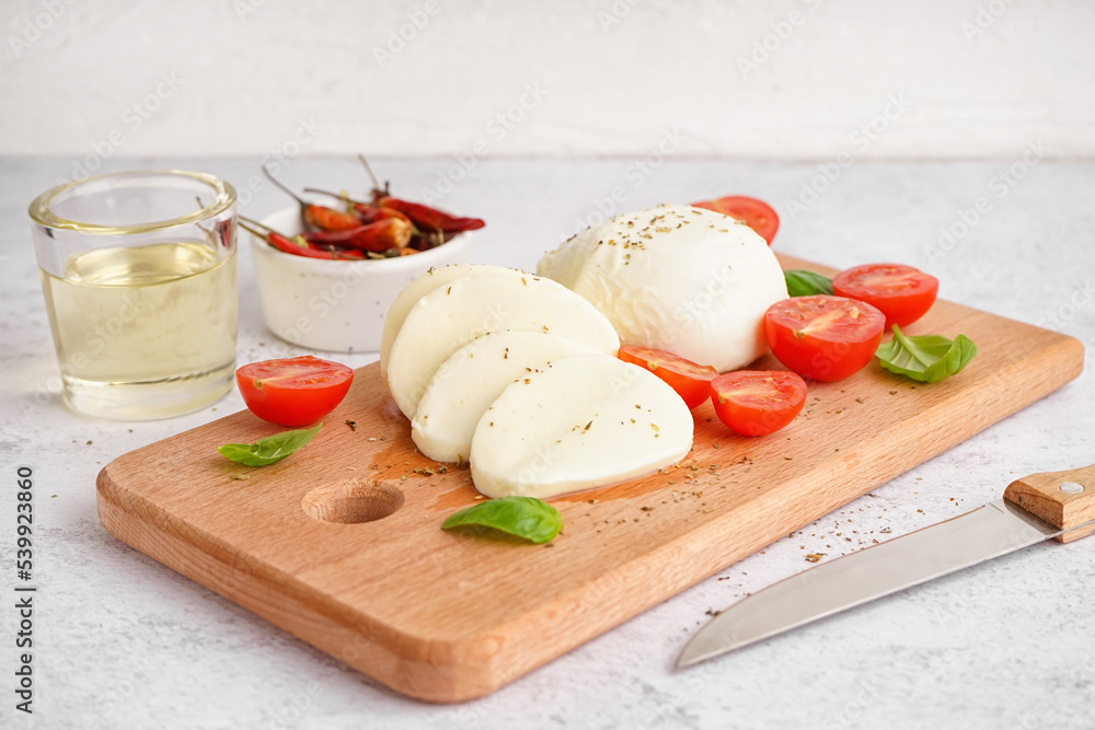 Wooden board with tasty mozzarella cheese and tomatoes on light background