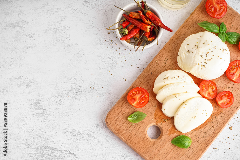 Wooden board with tasty mozzarella cheese and tomatoes on light background