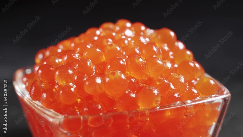 A serving of selected red caviar rotates on a black background in a transparent glass bowl. Gourmet 