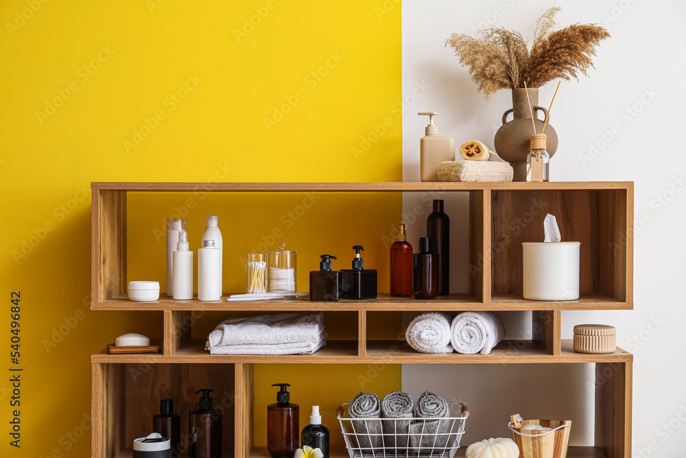 Shelf unit with different bath accessories near color wall