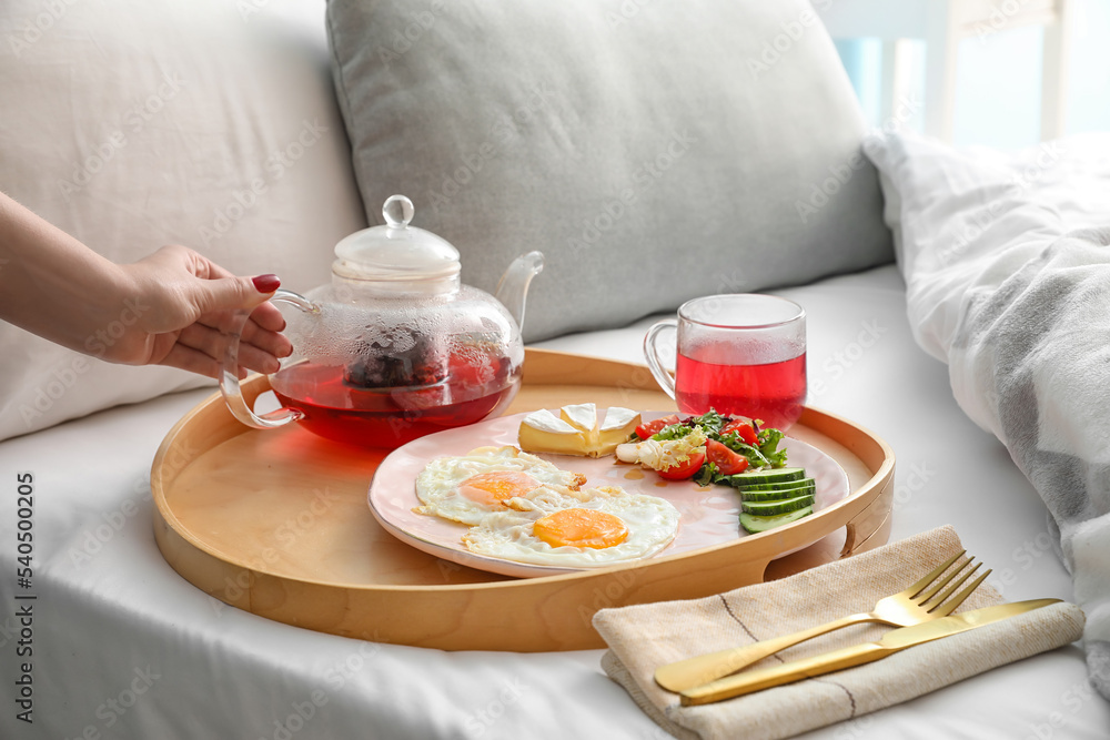 Female hand with teapot and tasty breakfast in bedroom