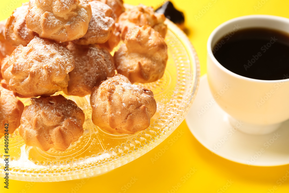 Dessert stand with delicious eclairs and cup of coffee on yellow background, closeup