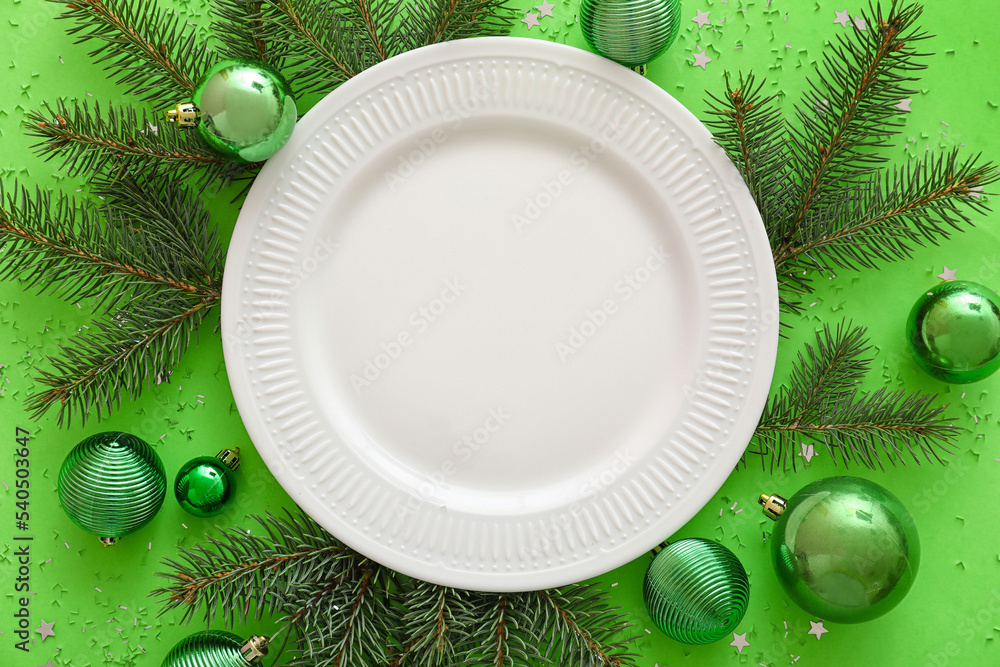 Composition with plate, fir branches and Christmas decorations on green background, closeup