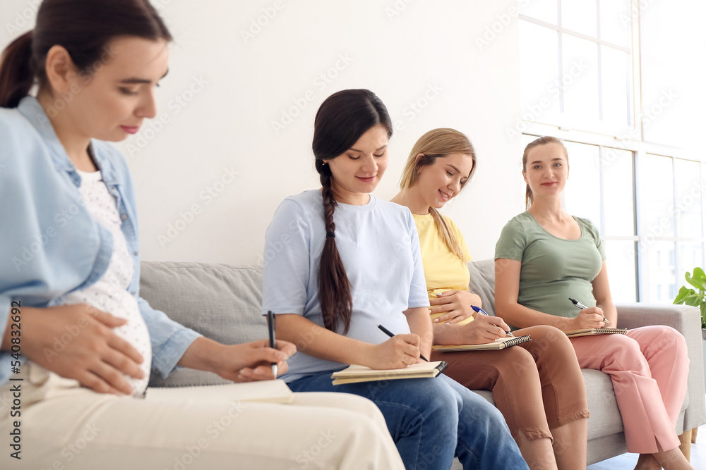 Young pregnant women writing in notebooks at course for expectant mothers