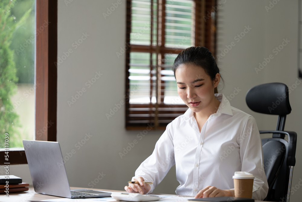 可爱的亚洲女人在办公室用笔记本电脑喝茶