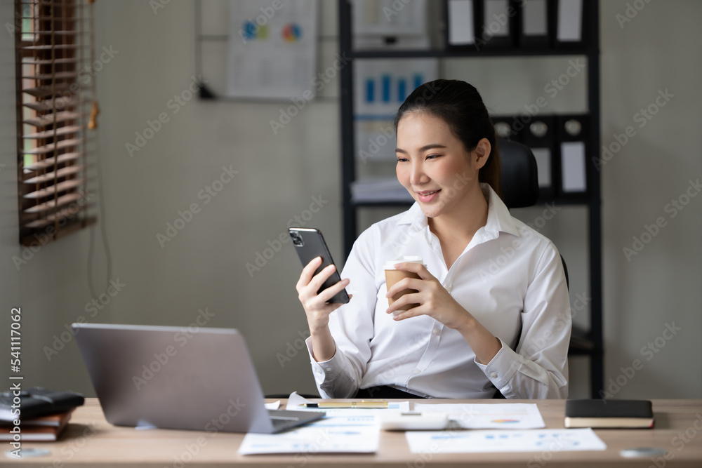 可爱的亚洲女人在办公室用笔记本电脑喝茶