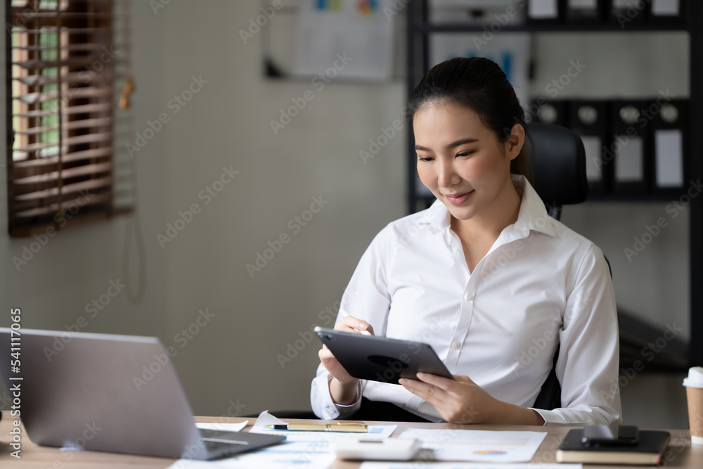 微笑的女人站在办公室用平板电脑浏览互联网或购物，快乐满足的年轻女性