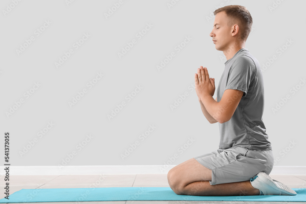 Young man meditating on mat near light wall