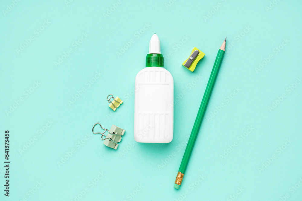 Bottle of glue, sharpener, paper clips and pencil on color background