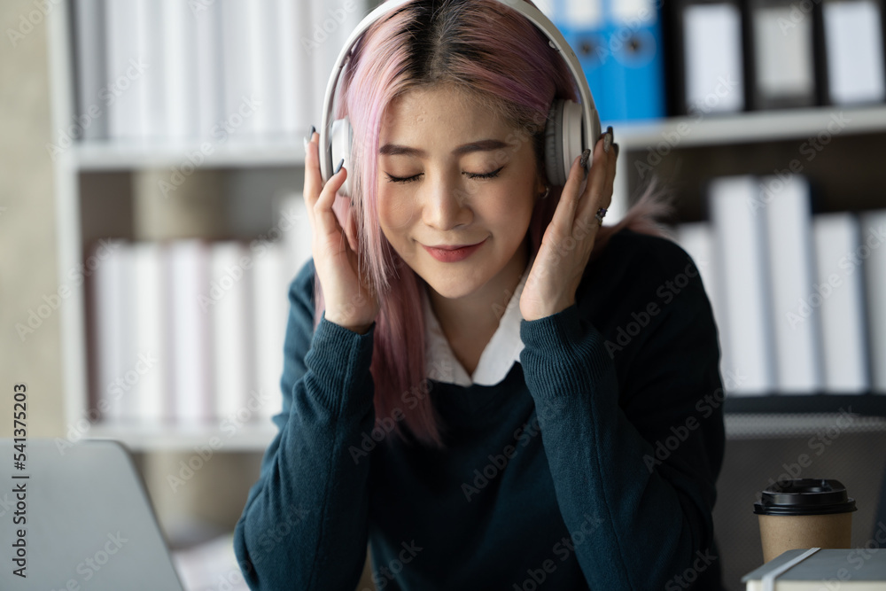 一位年轻的女学生坐在桌子旁，学习时使用耳机。