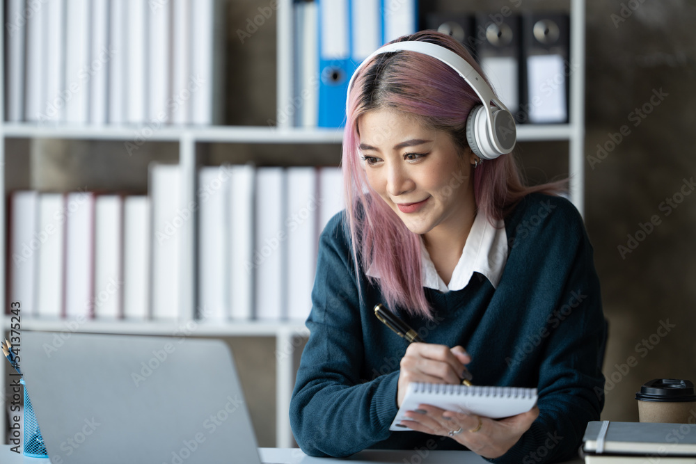 一位年轻的女学生坐在桌子旁，学习时使用耳机。