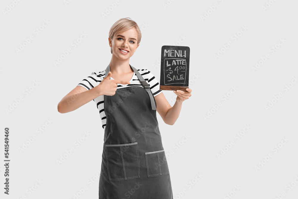 Female barista pointing at chalkboard with menu on light background