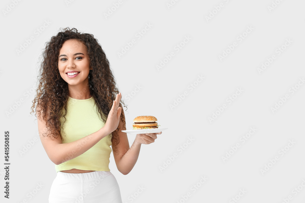 年轻的非裔美国女性拒绝在浅色背景下吃汉堡。饮食概念