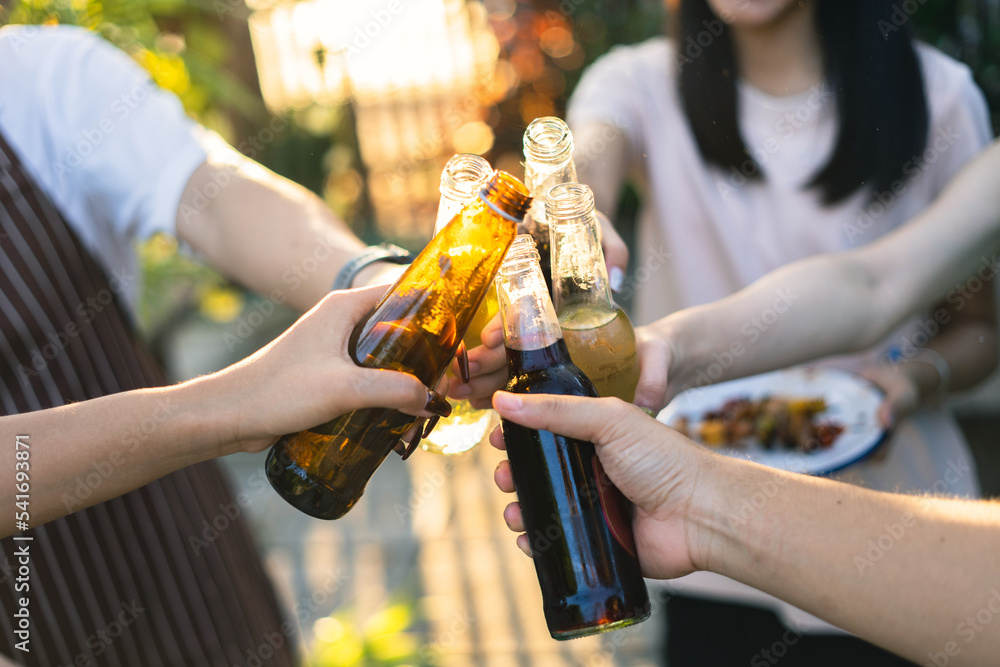 A group of Asian friends clinks a wine bottle during a party barbecue.