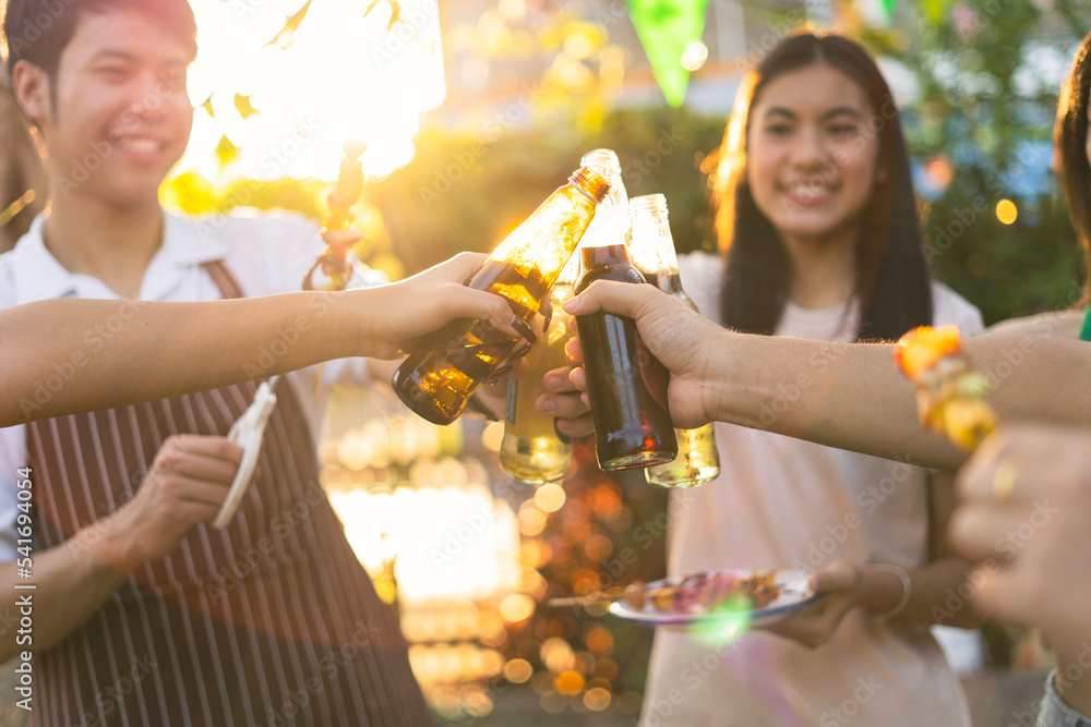 A group of Asian friends clinks a wine bottle during a party barbecue.