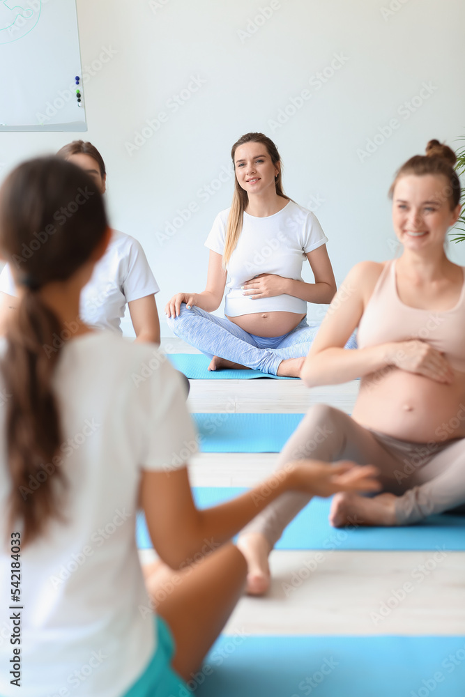 Young pregnant women doing yoga with coach in gym