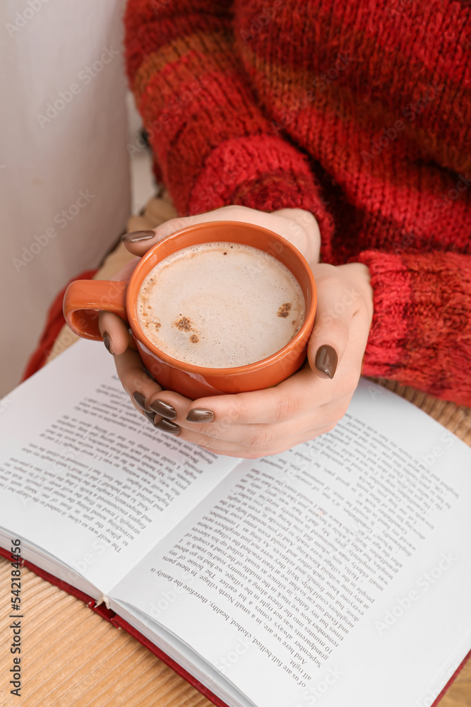 Woman with cup of coffee reading book, closeup