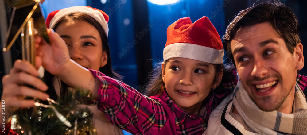 Caucasian couple and young daughter decorating Christmas tree at home.	 