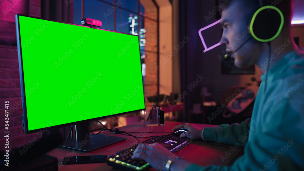 Excited Gamer Playing Online Video Game with a Mock Up Green Screen on His Powerful Personal Compute