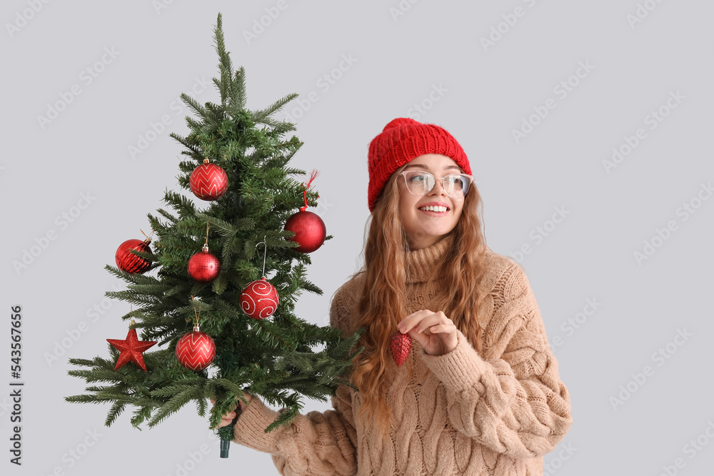 Young woman with Christmas tree and decor on grey background